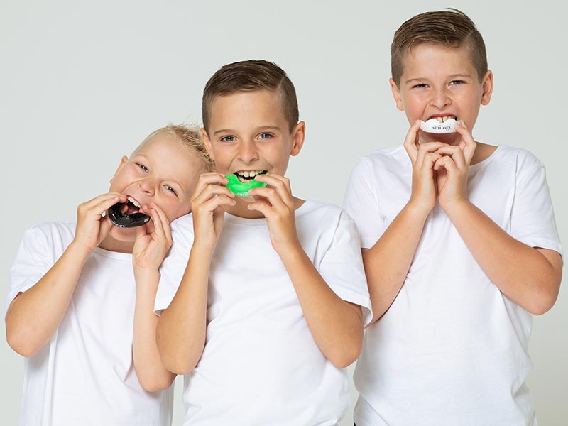 Three young boys putting their mouthguards on